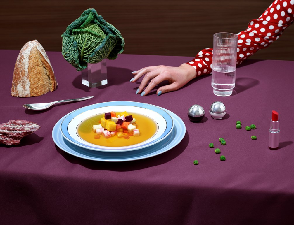 Hånd i hvitprikket bluse ved suppeskål og kålhode